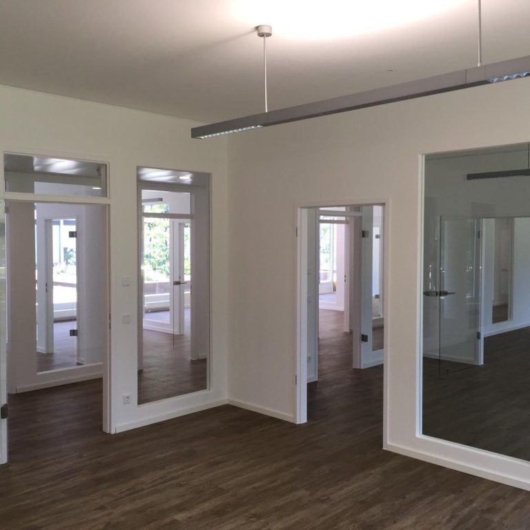 Umbau Wetter.com durch TTB München Heller Raum mit Holzfußboden und mehreren großen Fenstern in den Wänden.